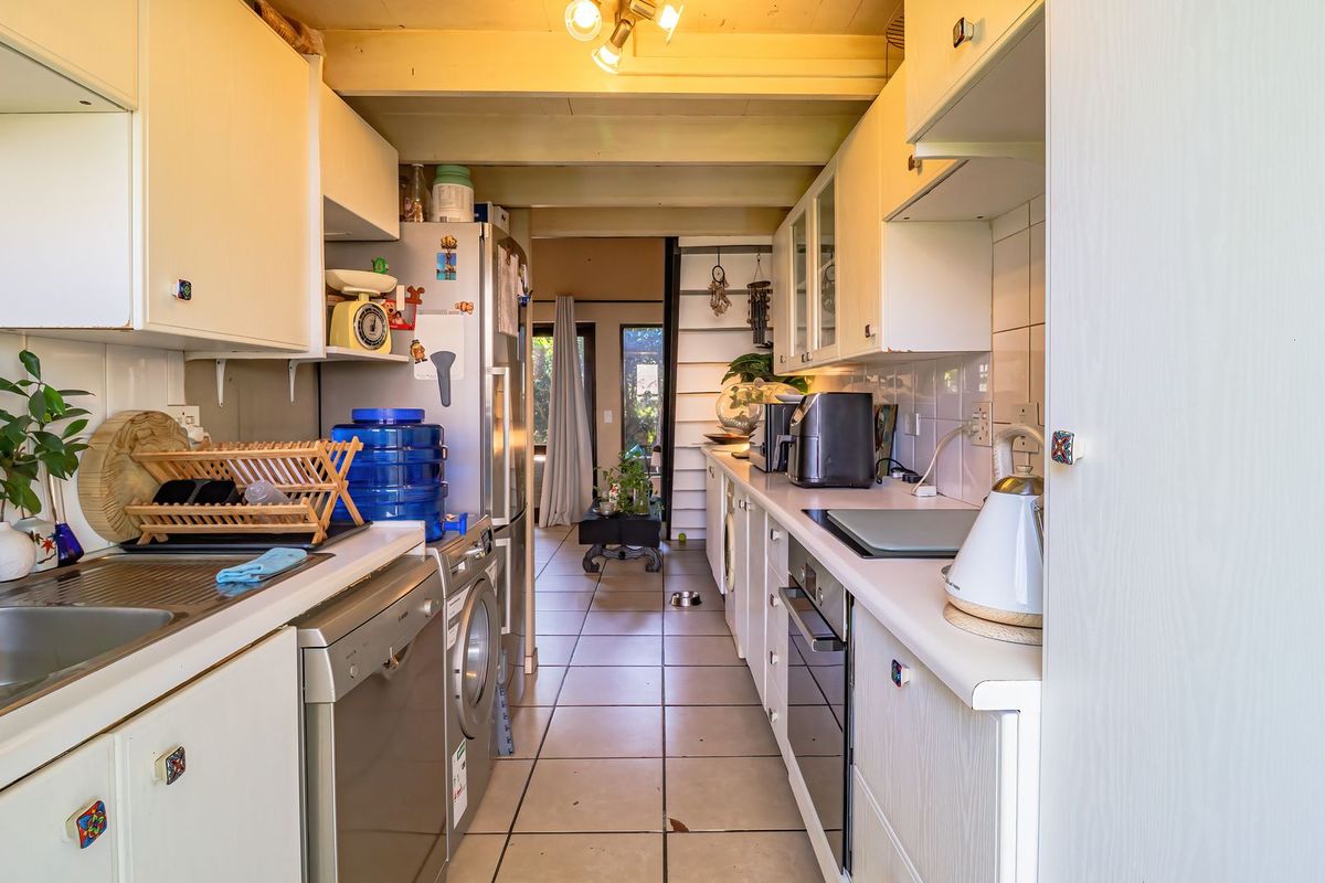 A galley-style kitchen featuring white cabinetry, tiled flooring, built-in oven, and cooktop, with a functional layout leading toward an open living area.