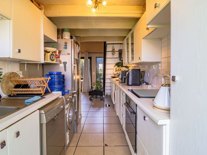 A galley-style kitchen featuring white cabinetry, tiled flooring, built-in oven, and cooktop, with a functional layout leading toward an open living area.