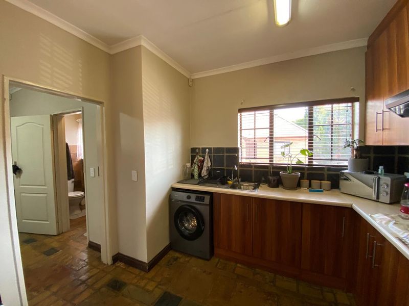Functional kitchen featuring wooden cabinetry, laminate countertops, a tiled backsplash, and dedicated plumbing for a washing machine, with an adjacent view into the bathroom.