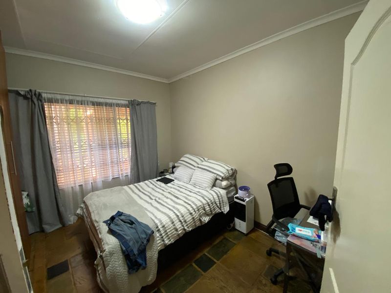 A functional bedroom featuring tiled flooring, a security gate on the window, and neutral wall finishes, offering a comfortable and practical living space.