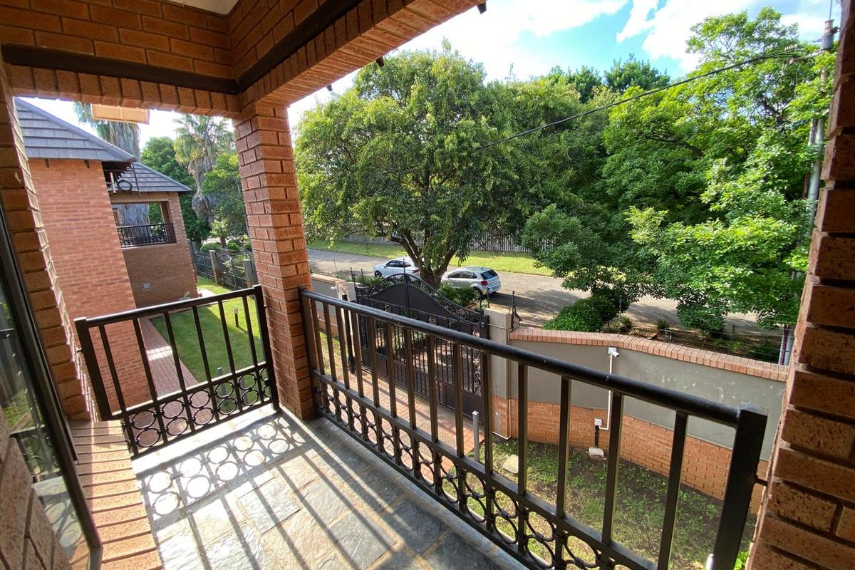 A covered balcony featuring brick pillars, stone flooring, and a metal balustrade, overlooking the complex grounds and street.