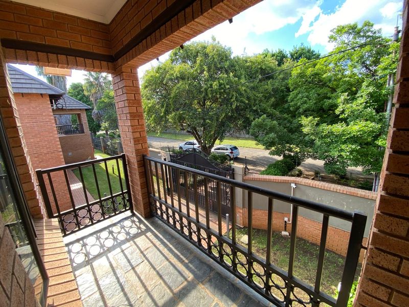 A covered balcony featuring brick pillars, stone flooring, and a metal balustrade, overlooking the complex grounds and street.
