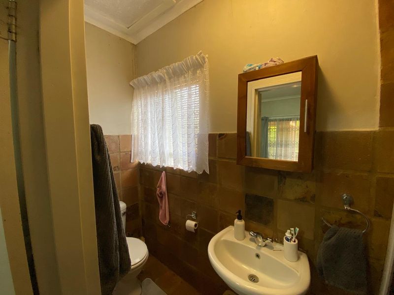 A compact bathroom featuring a wall-mounted basin, medicine cabinet, and ceramic wall tiling. The space would benefit from modern updates to finishes and fixtures.