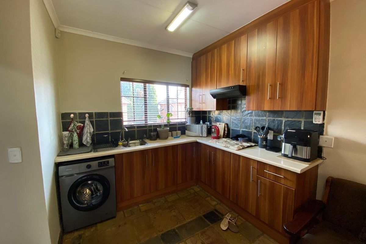A functional kitchen featuring wood-look cabinetry, stone tile backsplash, and integrated laundry plumbing, offering a practical layout with ample storage space.