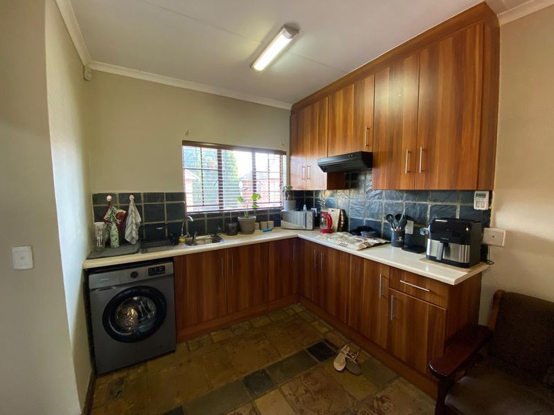A functional kitchen featuring wood-look cabinetry, stone tile backsplash, and integrated laundry plumbing, offering a practical layout with ample storage space.