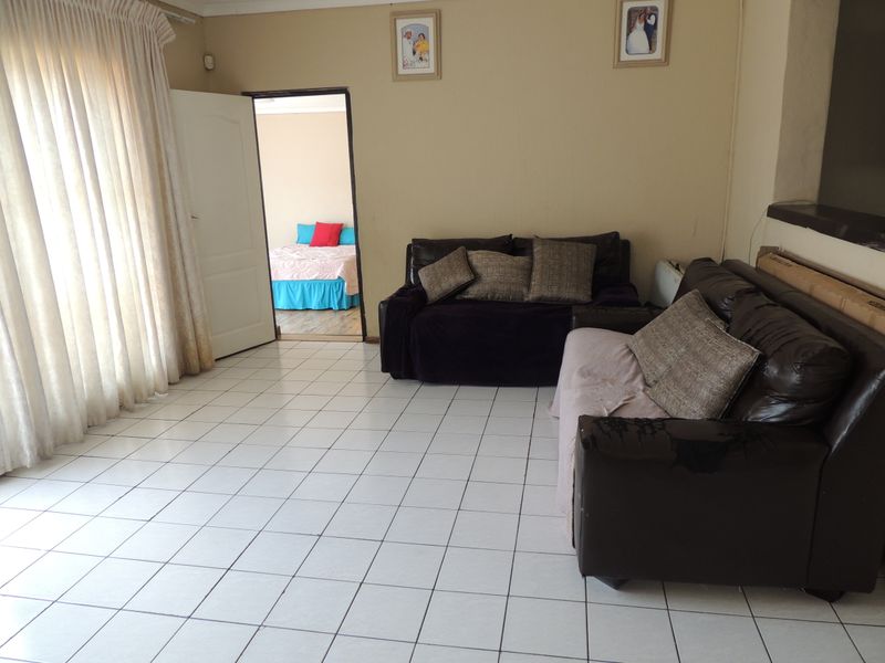 A living room area featuring neutral wall tones and white tiled flooring, with direct access to an adjacent bedroom.