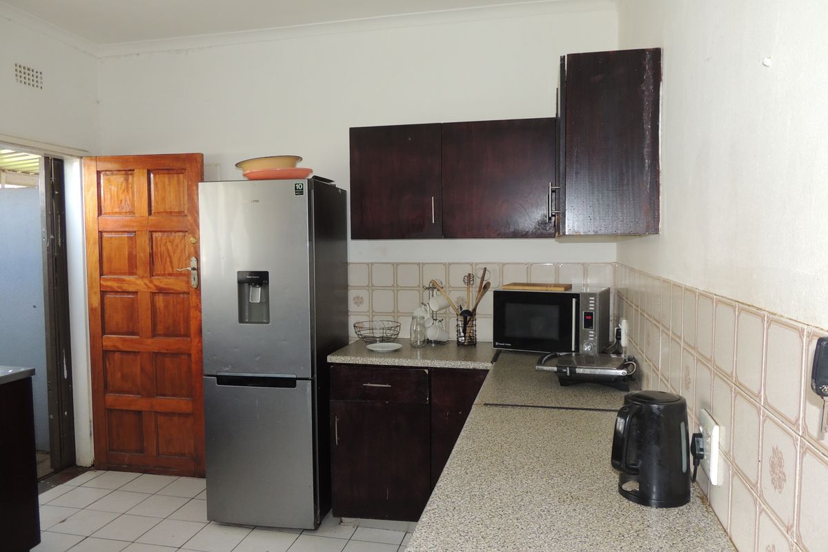 A functional kitchen featuring dark wood cabinetry, laminate countertops, and a tiled backsplash, providing a practical workspace with direct access to an exterior area.