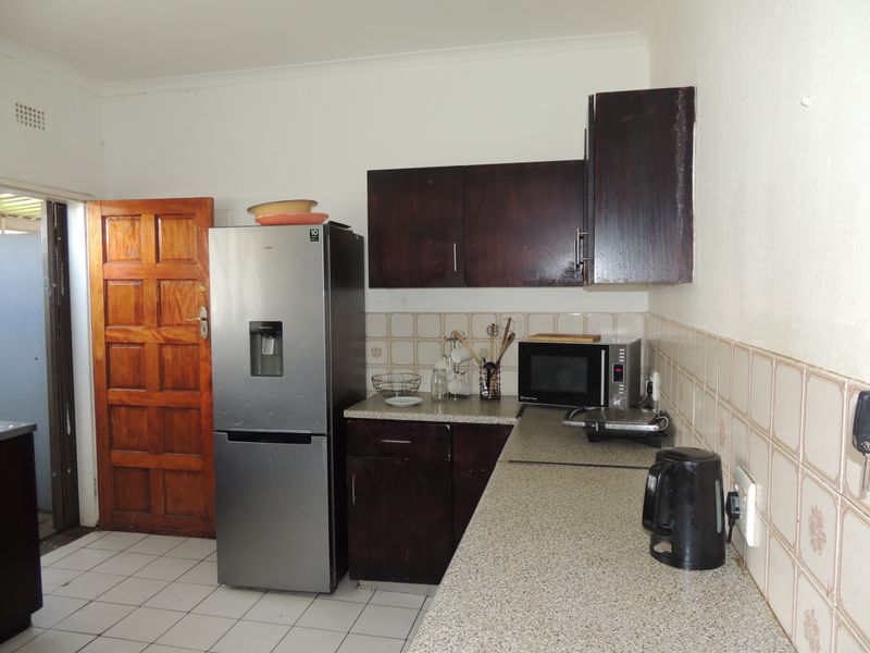 A functional kitchen featuring dark wood cabinetry, laminate countertops, and a tiled backsplash, providing a practical workspace with direct access to an exterior area.