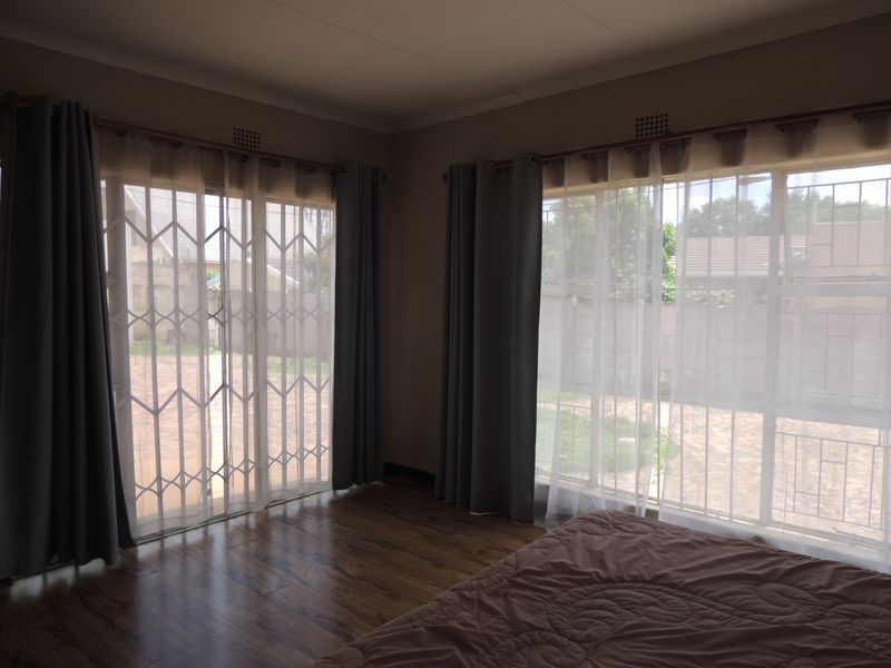 A bedroom featuring laminate flooring, large sliding doors with security gates, and natural light, offering a comfortable and functional living space.