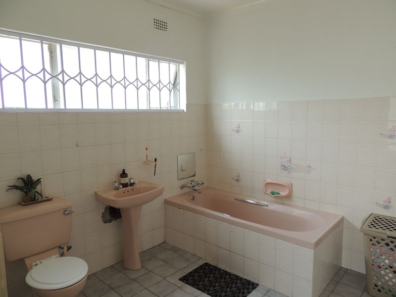 A dated bathroom featuring a pink pedestal basin, matching bathtub, toilet, and neutral wall tiling with decorative accents.