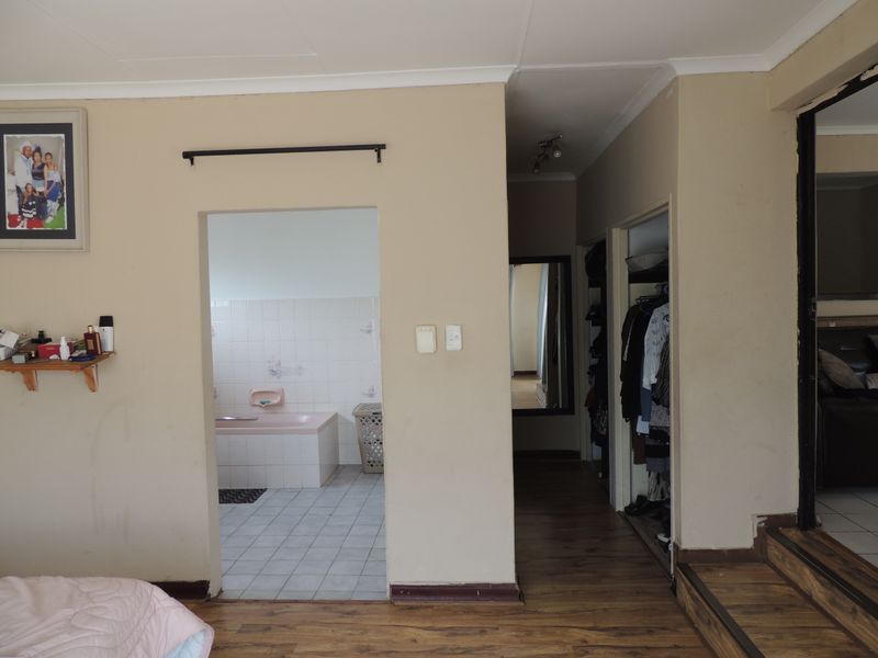Bedroom featuring laminate flooring, built-in cupboards, and an adjoining bathroom with a built-in bathtub and tiled finishes.