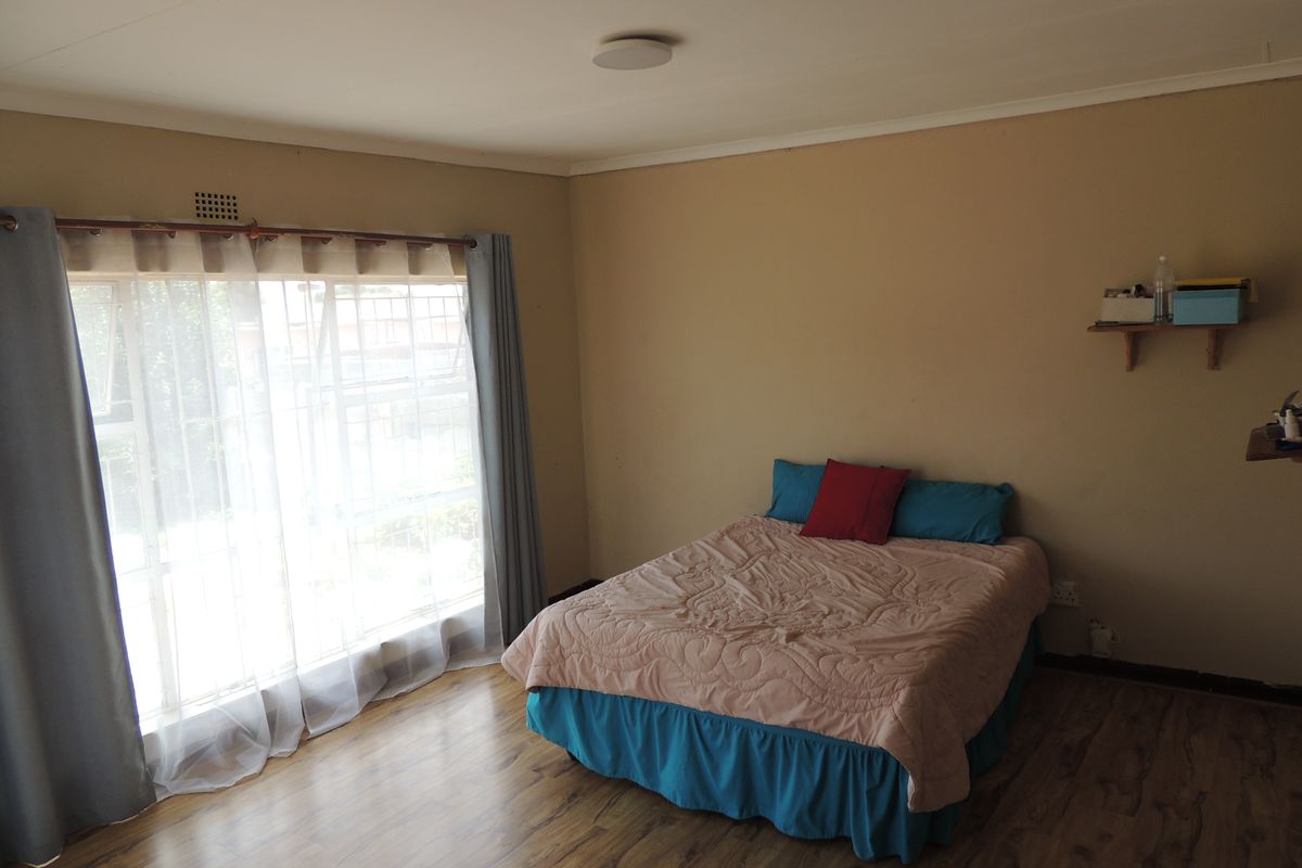 A bedroom featuring laminate flooring, a large window with security bars, and neutral wall tones, offering a functional space ready for personalization.