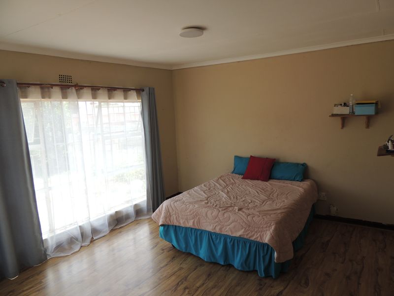 A bedroom featuring laminate flooring, a large window with security bars, and neutral wall tones, offering a functional space ready for personalization.