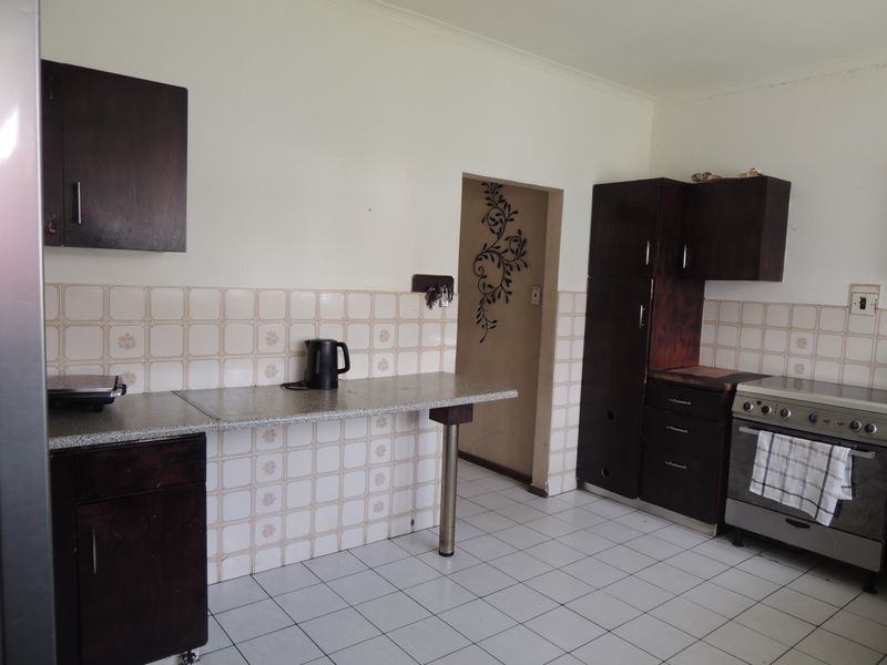 A functional kitchen featuring dark wood cabinetry, laminate countertops, tiled backsplash, and built-in oven and hob, offering potential for modern updates.