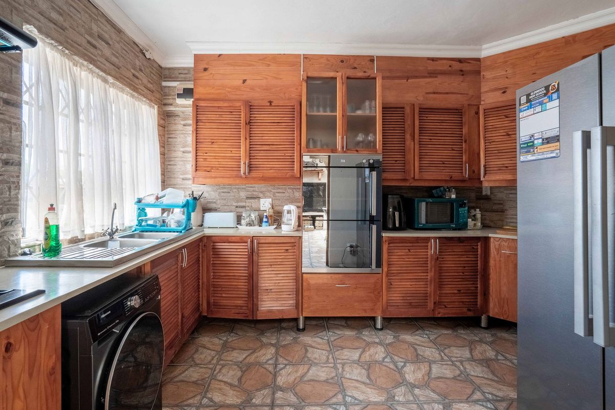 A functional kitchen featuring wooden cabinetry, built-in oven, stainless steel sink, and stone-look tile flooring with a tiled backsplash.