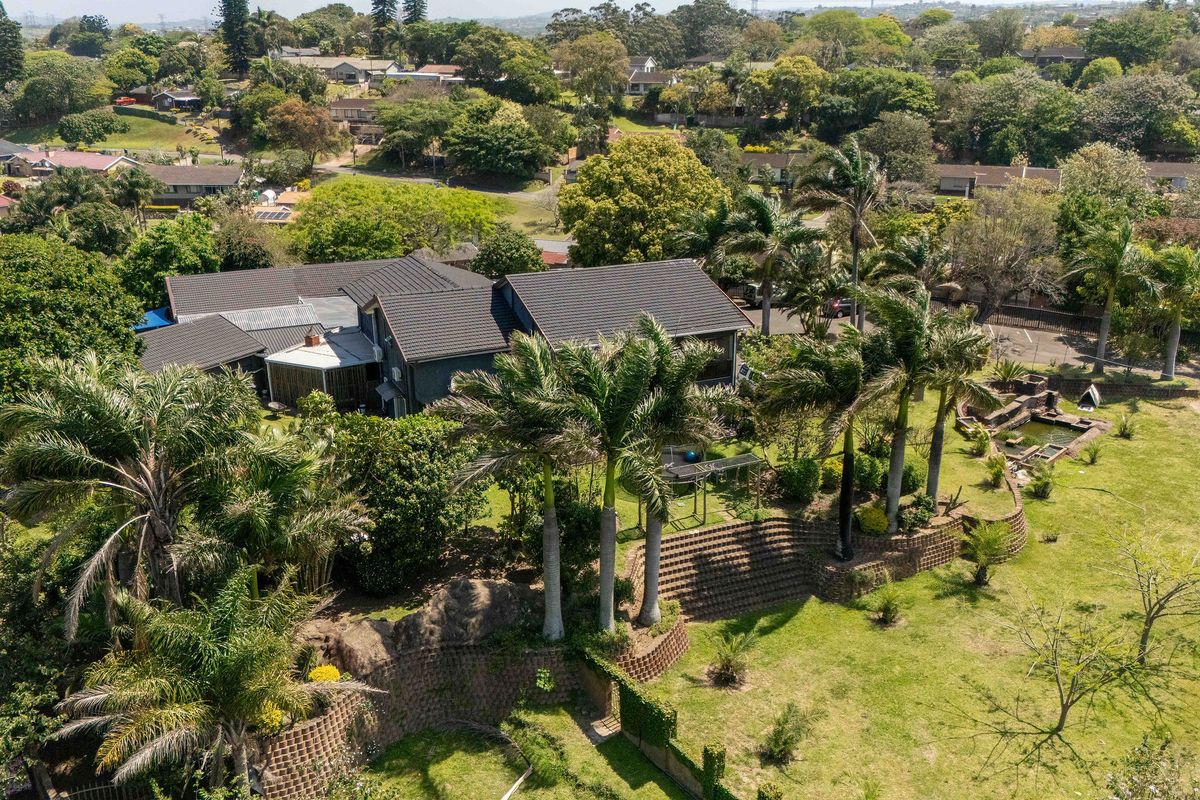 Aerial view of a residential property featuring a large landscaped garden, mature palm trees, and tiered retaining walls surrounding the main dwelling.
