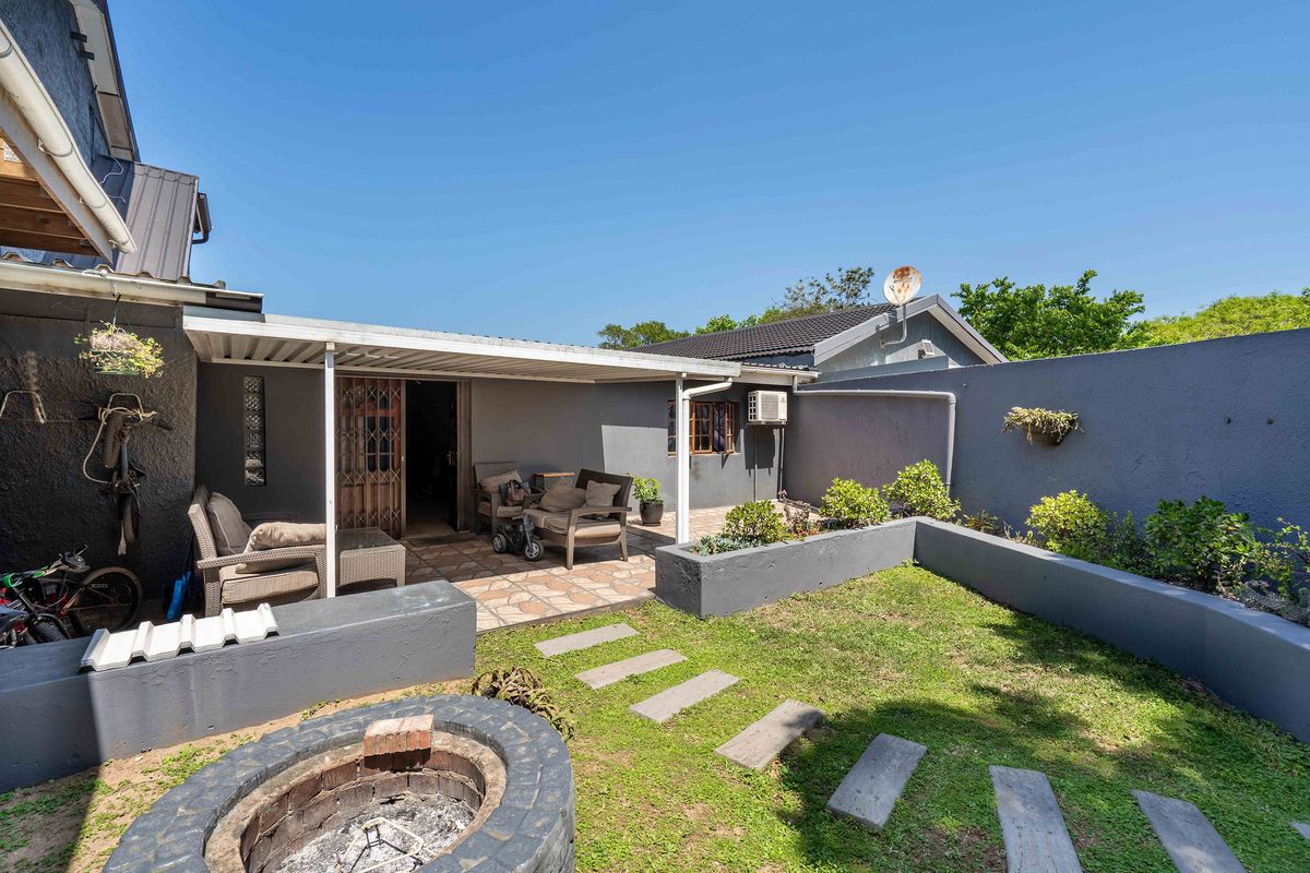 Rear exterior area featuring a covered patio, built-in fire pit, raised garden beds, and paved pathways, offering a functional outdoor entertainment space.