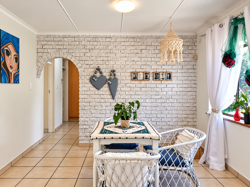 A bright dining area featuring a distinctive white-painted exposed brick feature wall, an arched entryway, and neutral ceramic floor tiles.