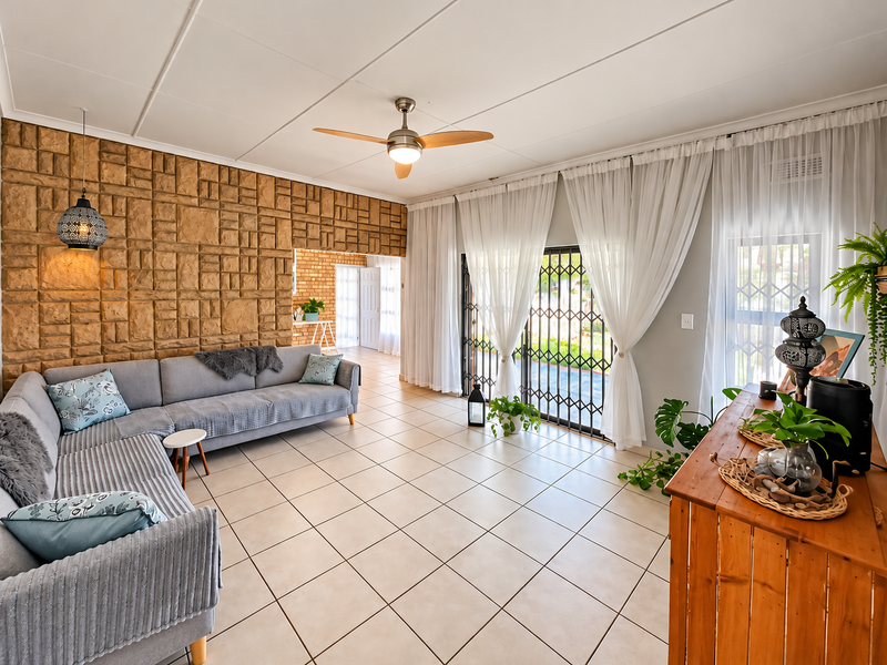 Spacious living room featuring a unique textured stone feature wall, neutral tiled flooring, and large sliding doors providing access to the outdoor area.