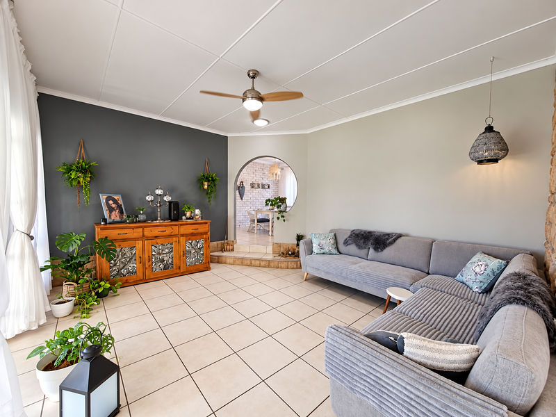 Spacious living room featuring tiled flooring, a ceiling fan, and a distinctive arched opening leading to the adjacent dining area.