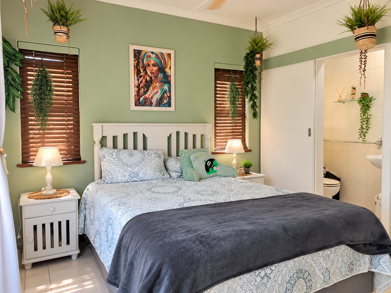 A well-maintained bedroom featuring sage green walls, wooden venetian blinds, and direct access to an en-suite bathroom with tiled flooring.