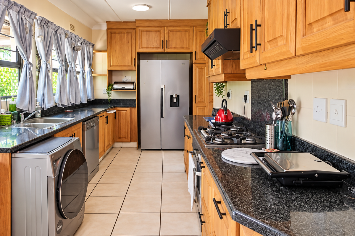 A functional kitchen featuring warm wooden cabinetry, granite countertops, a gas hob, and integrated appliances with tiled flooring throughout.