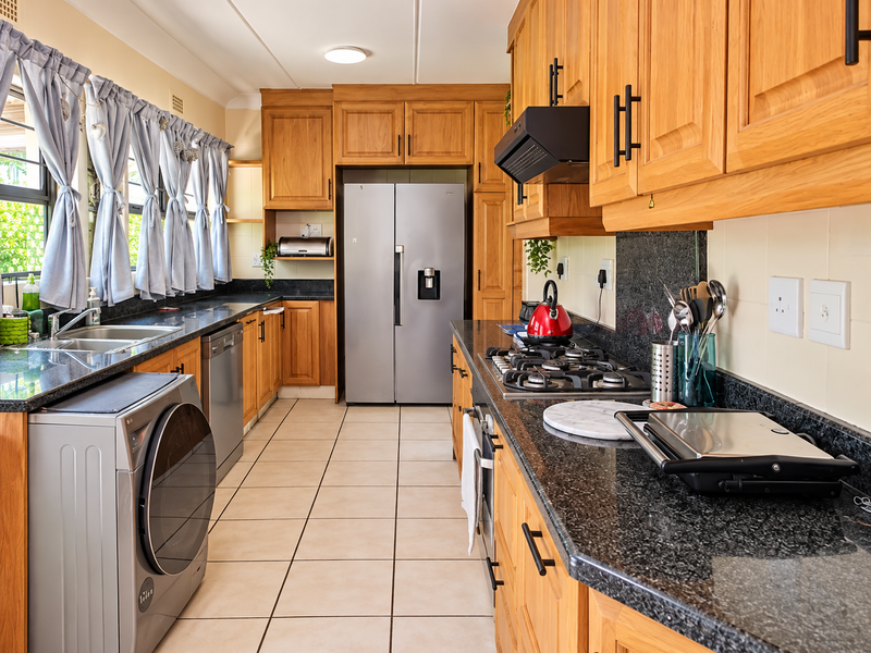 A functional kitchen featuring warm wooden cabinetry, granite countertops, a gas hob, and integrated appliances with tiled flooring throughout.