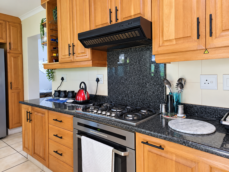 A well-maintained kitchen featuring solid wood cabinetry, granite countertops, a gas hob, and a built-in oven with a modern extractor fan.