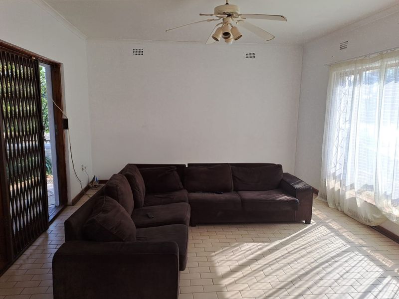 A living room featuring tiled flooring, a ceiling fan, and a sliding door with a security gate leading to the exterior.