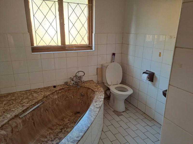 A dated bathroom featuring a built-in bathtub, toilet, and tiled finishes. The space requires cosmetic updates and repairs to the tiling and fixtures.