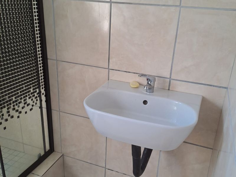 A functional bathroom featuring a wall-mounted basin with chrome tapware, tiled wall and floor finishes, and an adjacent shower enclosure.