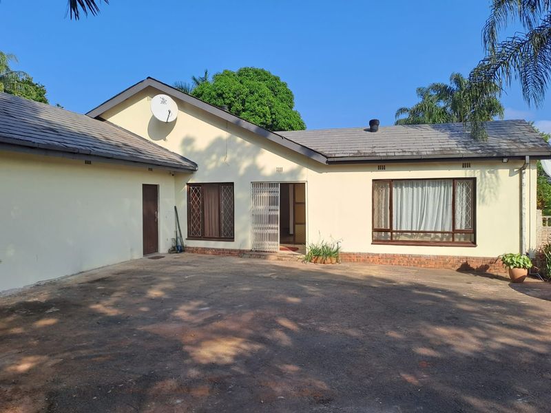 Front exterior view of a single-story house featuring a tiled roof, paved driveway, and security gate entrance.