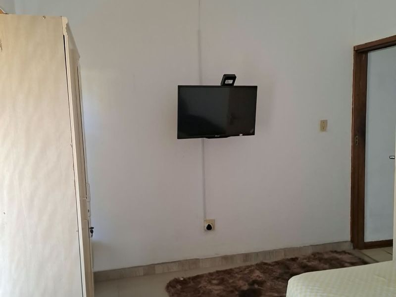 A bedroom featuring tiled flooring and wall-mounted television with visible electrical conduit.