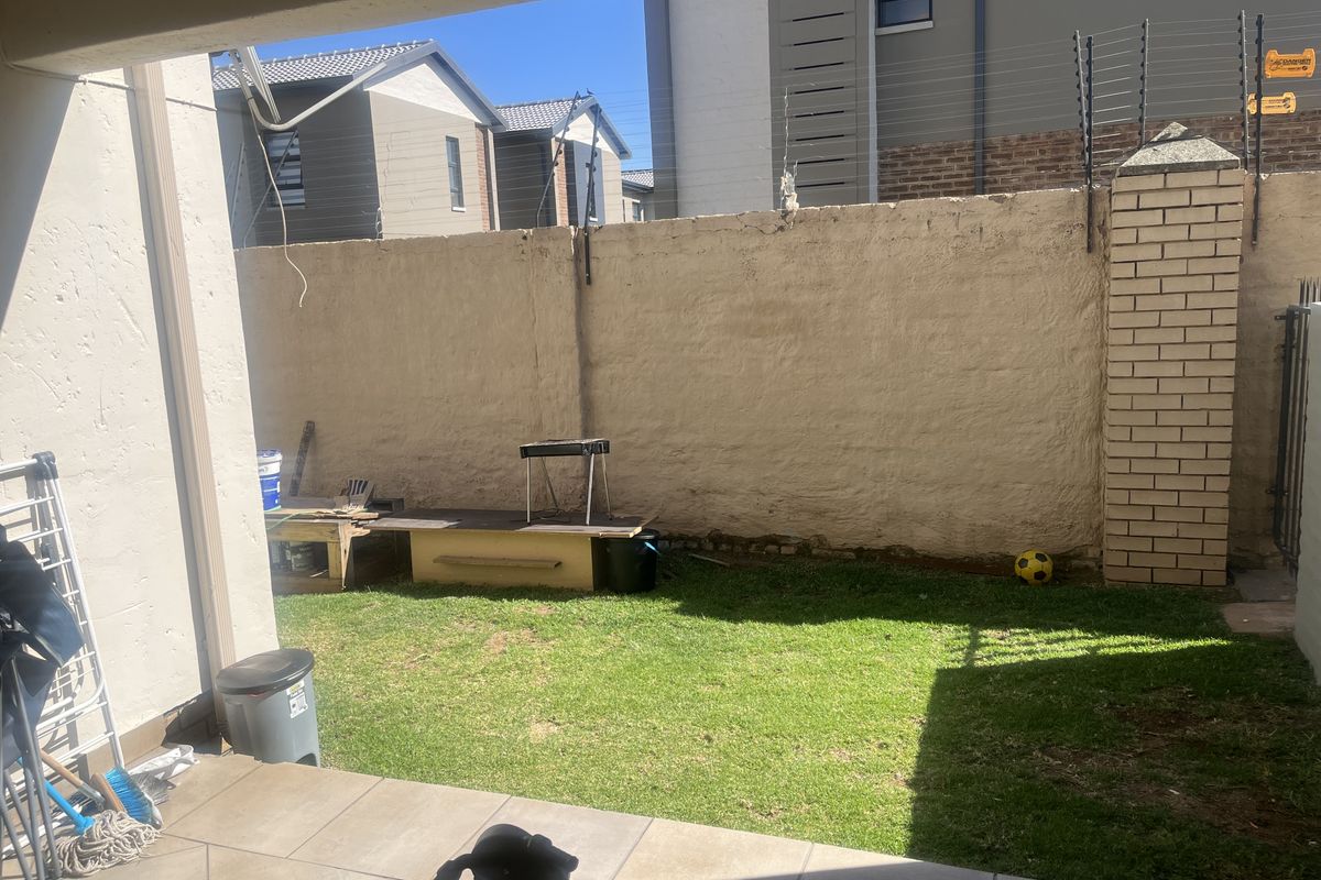 A small rear garden featuring a tiled patio area, a lawn, and a boundary wall with electric fencing.