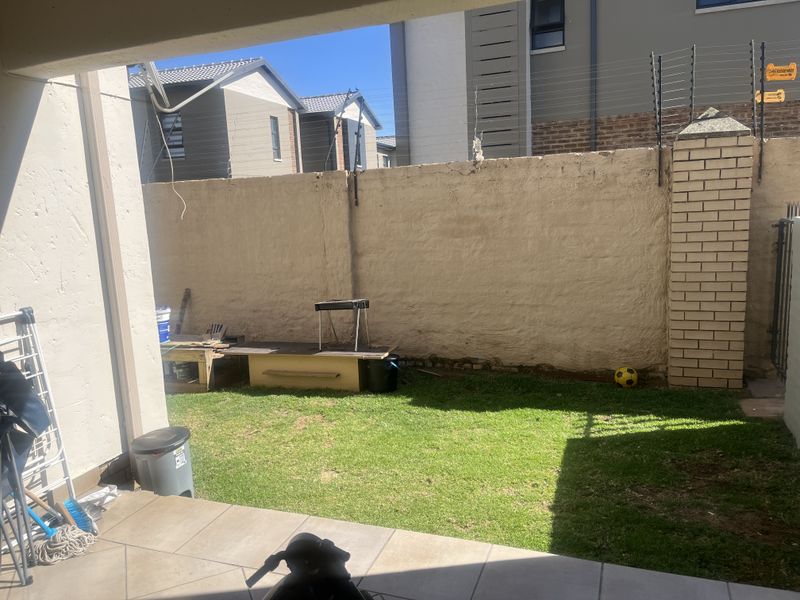 A small rear garden featuring a tiled patio area, a lawn, and a boundary wall with electric fencing.