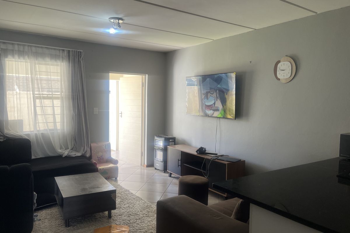 A functional living room featuring tiled flooring and neutral wall finishes, providing a comfortable space with natural light from the adjacent window and doorway.