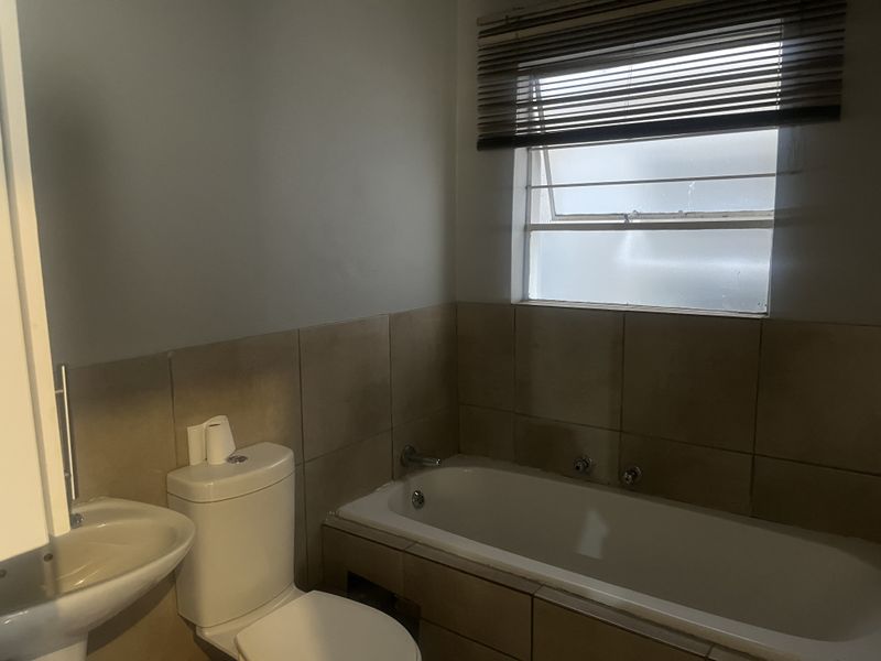 A functional bathroom featuring a bathtub, pedestal sink, and toilet with neutral wall tiling and window blinds for privacy.