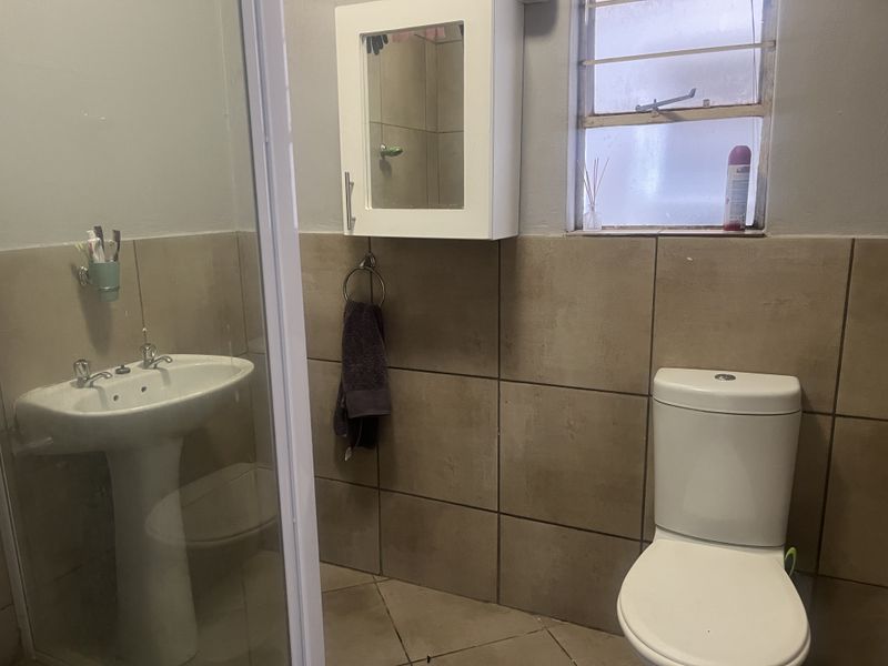 A functional bathroom featuring a pedestal basin, toilet, and shower enclosure with neutral wall tiling and a wall-mounted medicine cabinet.
