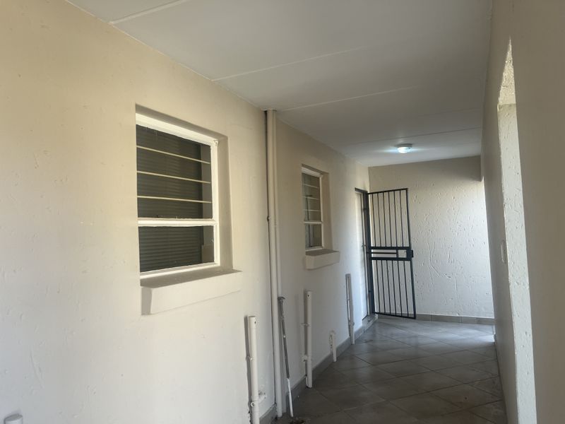 A covered exterior hallway or walkway featuring tiled flooring, security gates, and window security bars, showing signs of wear on the wall finishes.