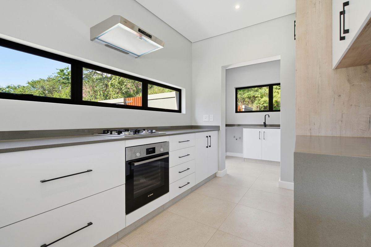 Modern kitchen featuring sleek white cabinetry, stone countertops, built-in oven, gas hob, and an adjoining scullery area with a sink.