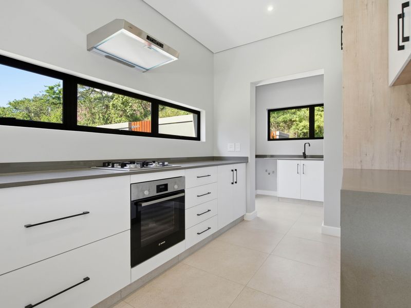 Modern kitchen featuring sleek white cabinetry, stone countertops, built-in oven, gas hob, and an adjoining scullery area with a sink.