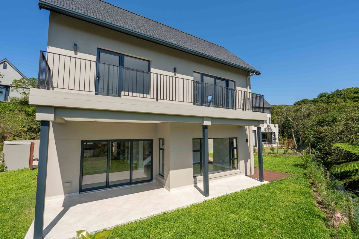 Rear view of a modern two-story house featuring a tiled ground-floor patio, an upper-level balcony with metal railings, and large sliding glass doors.