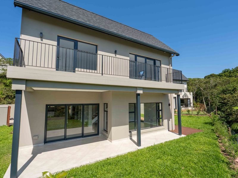 Rear view of a modern two-story house featuring a tiled ground-floor patio, an upper-level balcony with metal railings, and large sliding glass doors.
