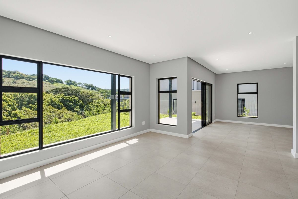A bright, modern, and spacious open-plan living area featuring large windows with scenic views, tiled flooring, and direct access to an outdoor patio.
