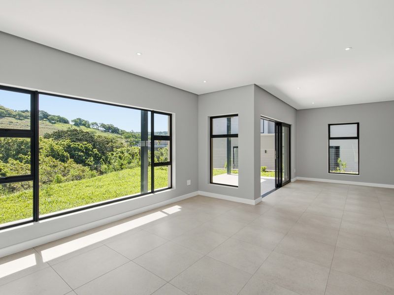 A bright, modern, and spacious open-plan living area featuring large windows with scenic views, tiled flooring, and direct access to an outdoor patio.