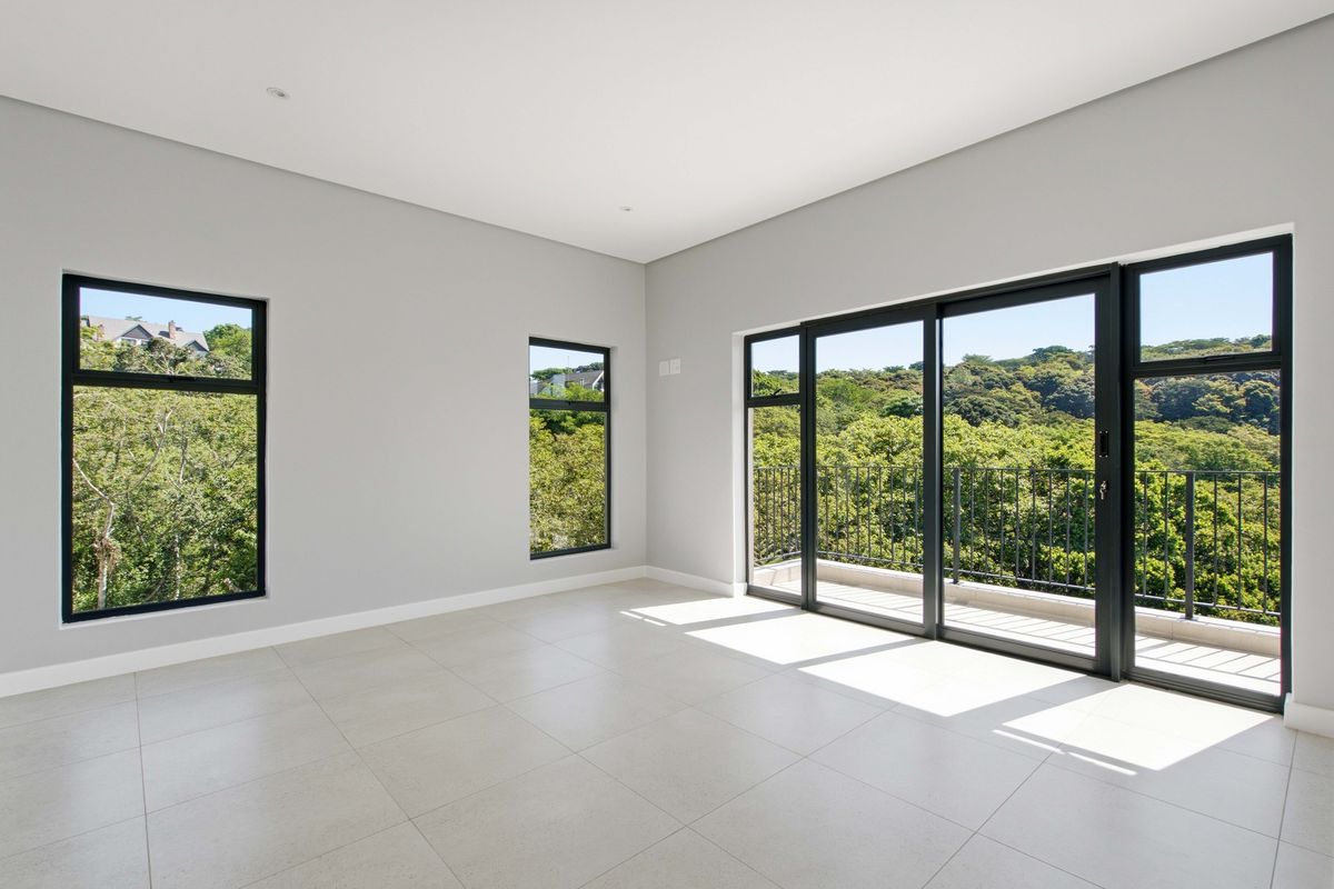 A bright, modern, and empty bedroom featuring large black aluminium windows and sliding doors that open onto a balcony with scenic green views.