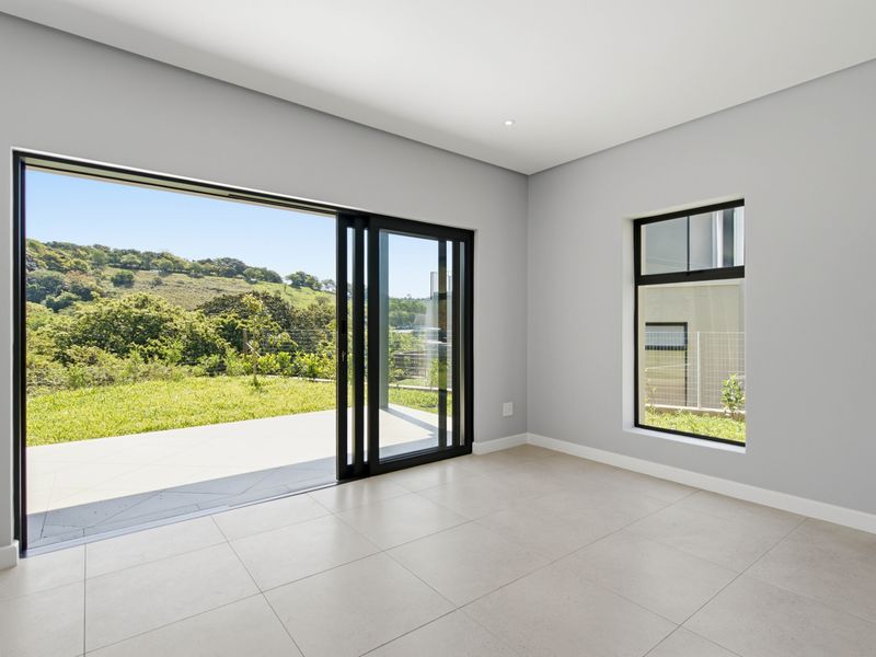A bright, modern, and empty living area featuring large sliding glass doors that open onto a patio with scenic green views.