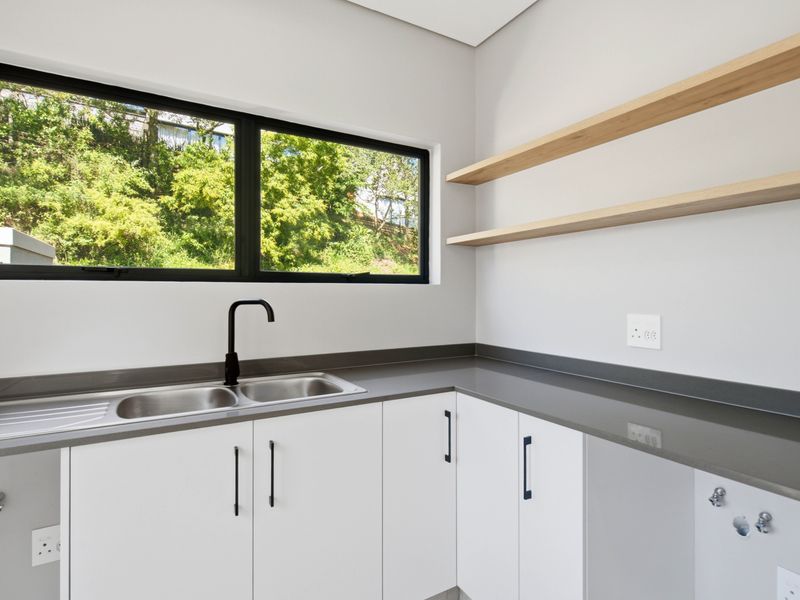 Modern laundry room featuring white cabinetry, grey stone countertops, a double sink with black tapware, and floating timber shelving.