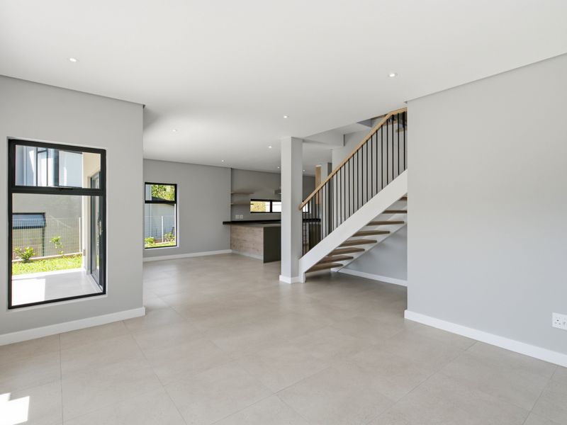 Spacious open-plan living area featuring modern tiled flooring, recessed lighting, and a contemporary staircase, seamlessly flowing into a sleek kitchen space.