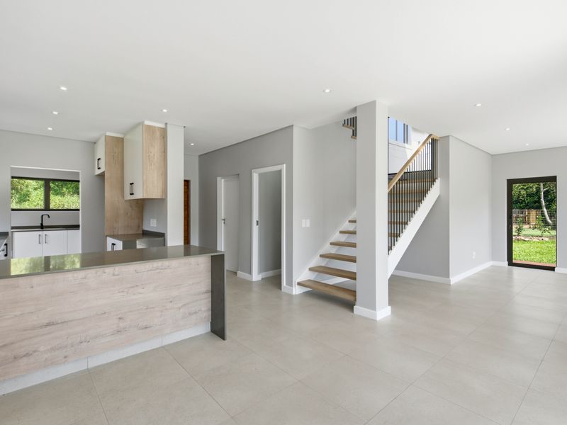 Modern open-plan living area featuring a sleek kitchen with stone countertops, tiled flooring, and a contemporary staircase with a metal balustrade.